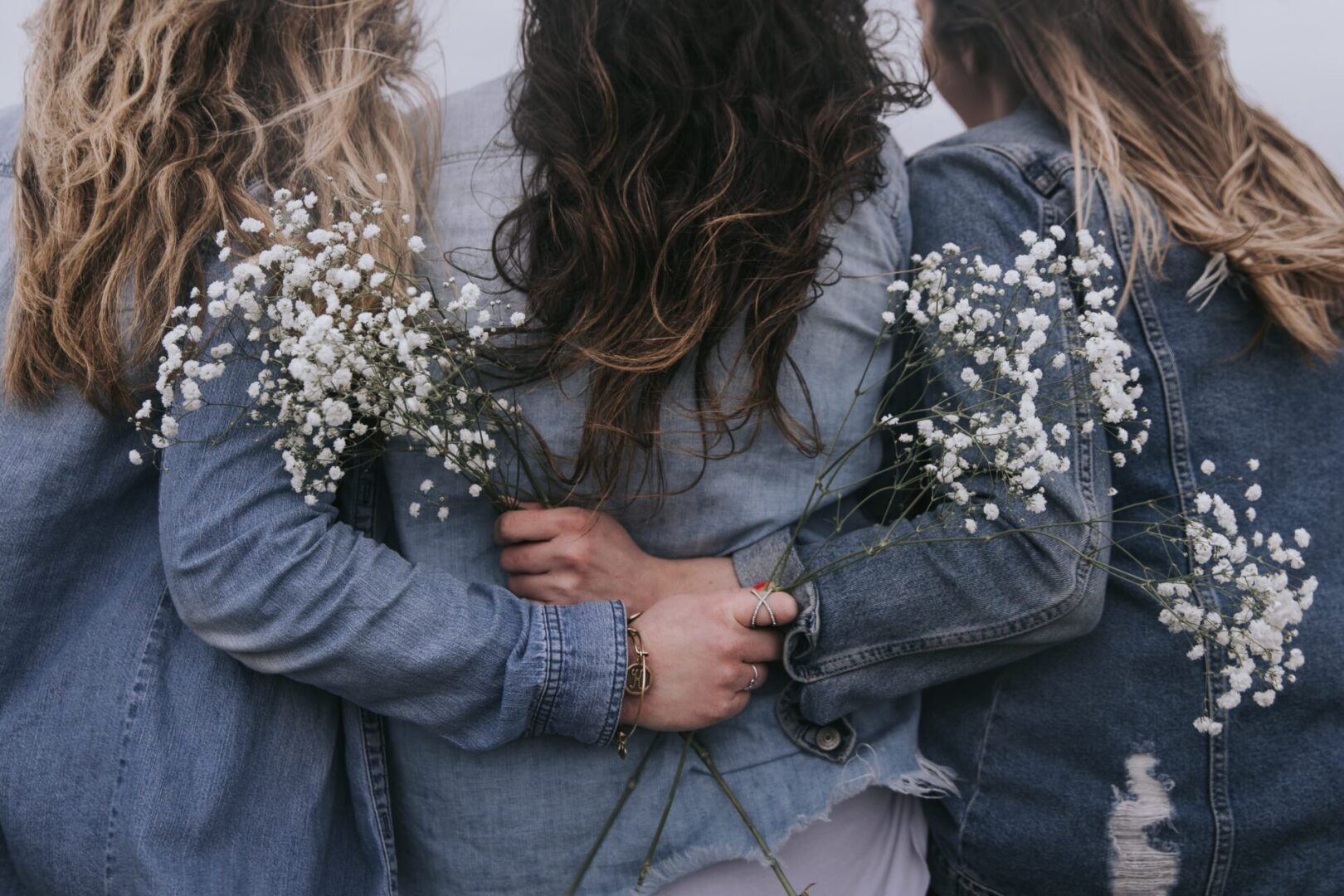 Three women in denim holding white flowers.